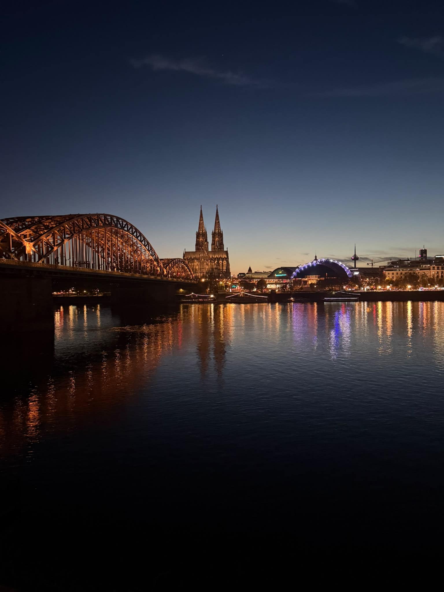 Kölsch-Tourbus Kölner Dom und Hohenzollernbrücke mit Spiegelungen im Rhein am Abend